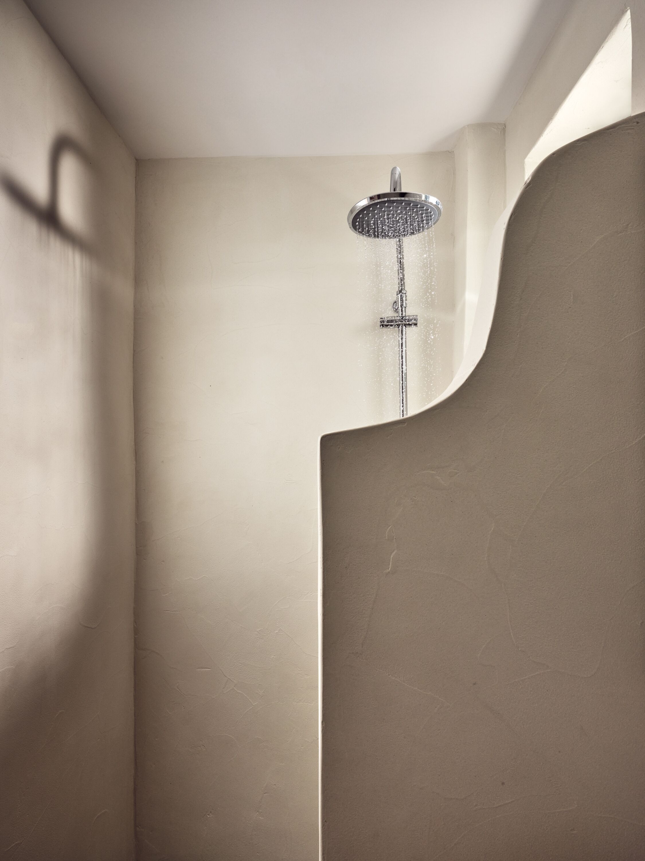 Een moderne douche met een wand in gebogen vorm, een zichtbare douchekop en een structuurwand.