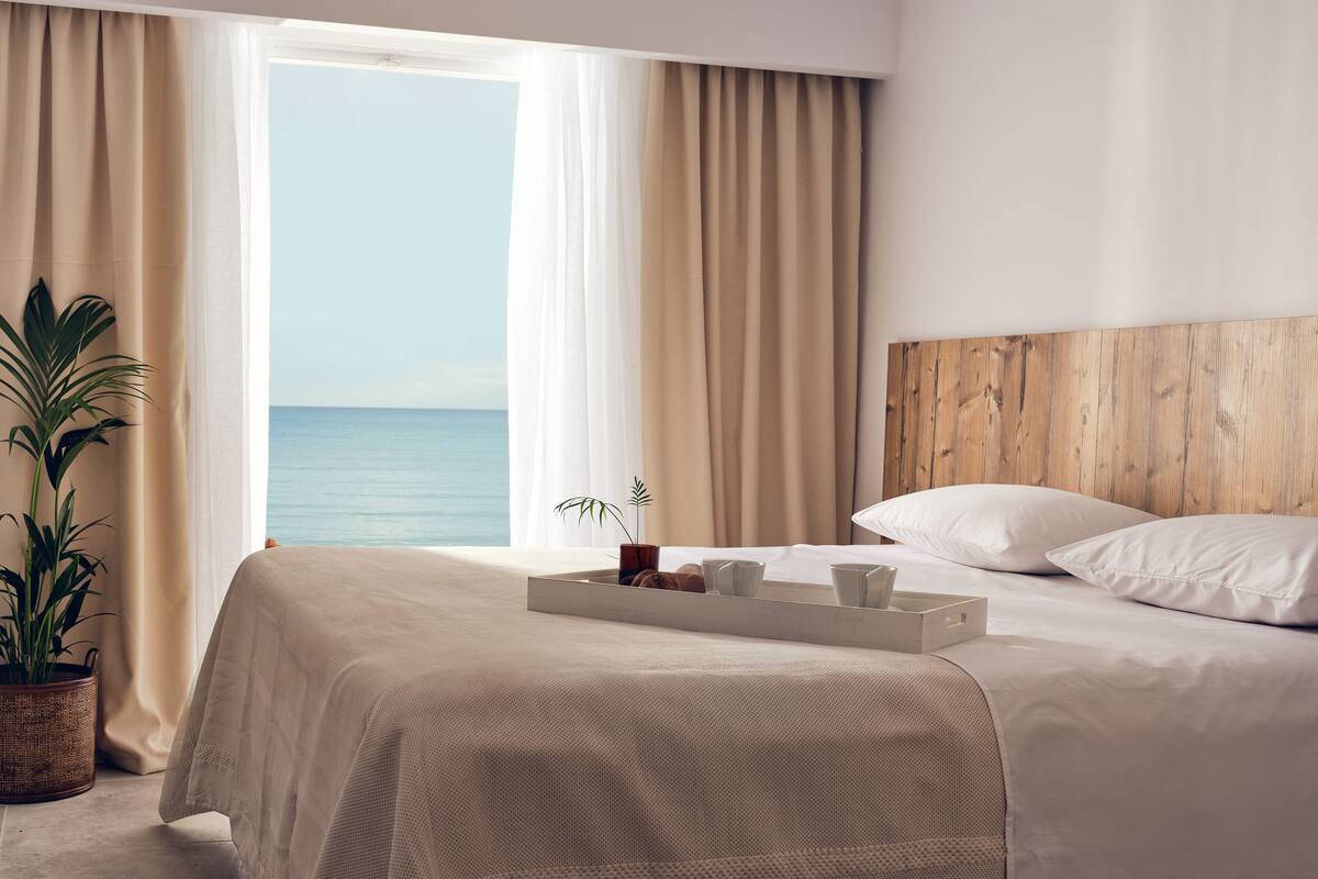 Une chambre d’hôtel avec un lit, un plateau contenant des articles pour le petit-déjeuner, une plante et une vue sur la mer.