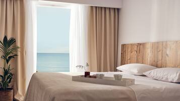 Habitación de hotel con una cama, una bandeja con alimentos para el desayuno, una planta y vistas al mar.