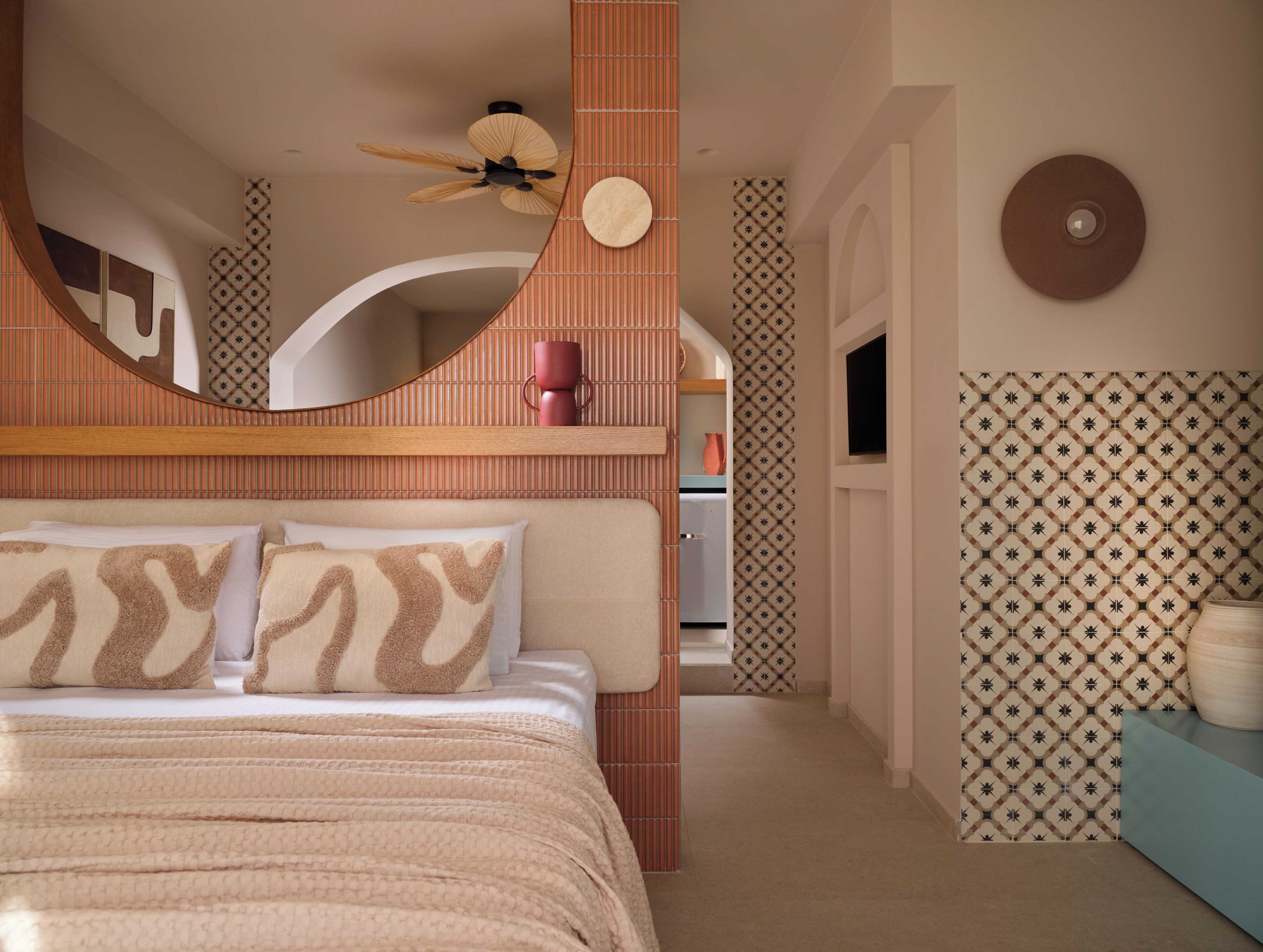 Un dormitorio con cama, almohadas, ventilador de techo, televisión y paredes con diseño.