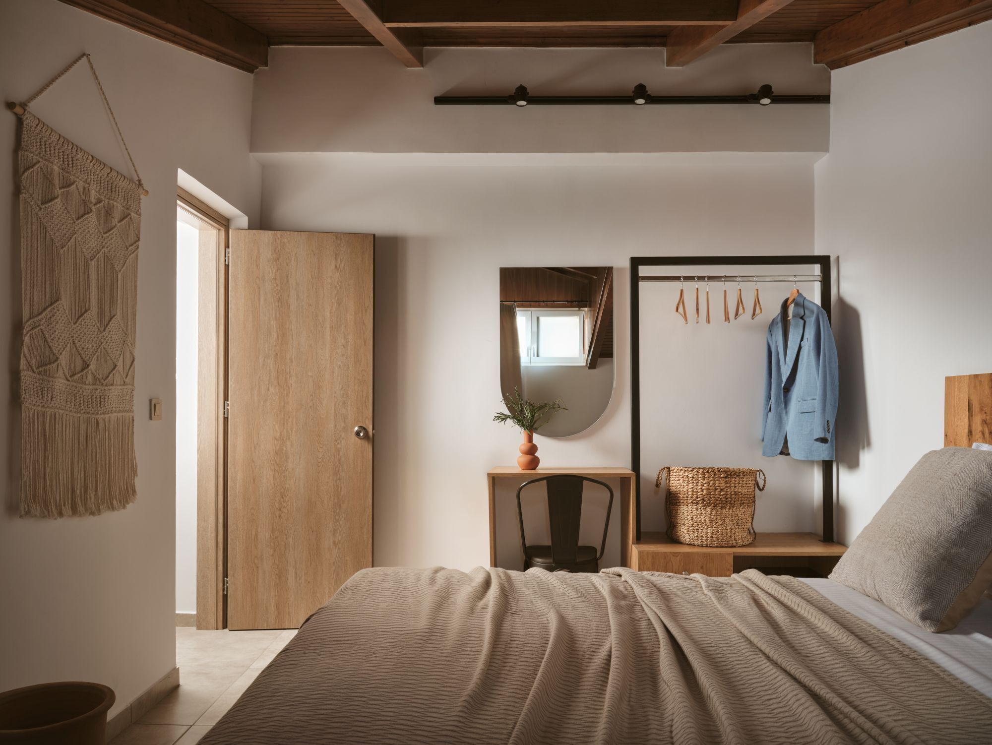 Un dormitorio con una cama, un armario de madera, un espejo, una mesita con una planta y un perchero.