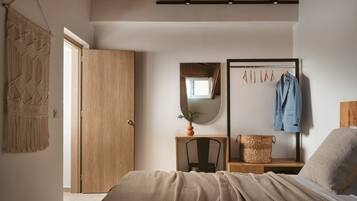 Un dormitorio con una cama, un armario de madera, un espejo, una mesita con una planta y un perchero.