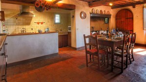 A rustic kitchen with a central island, wooden ceiling beams, and a dining area with a table set for six. - Cozy Farmhouse with Swimming Pool in Le Tolfe near Florence (Siena)