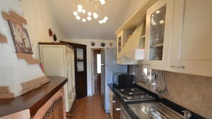 Una cocina con estufa, pileta y alacenas. Hay una puerta que da a otra habitación.