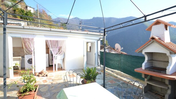 Un patio con mesa y sillas, un pequeño jardín y vistas a las montañas.