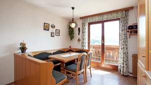 A dining area with a wooden table and benches, a hanging light fixture, and a view through a large window. - Apartment Near the ski Resort (Sankt Johann im Pongau)