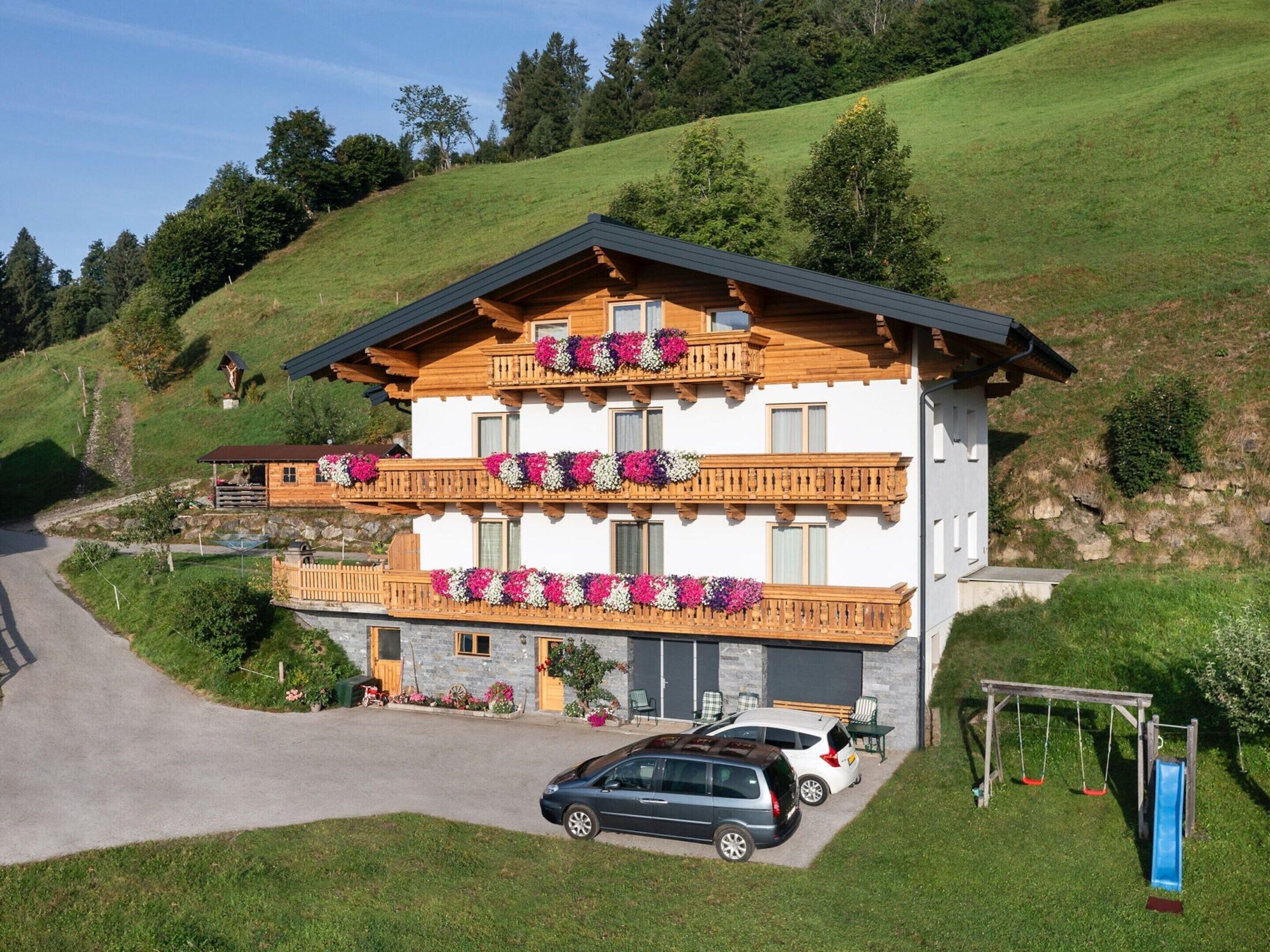 A two-story chalet with wooden balconies, a stone facade, and a car parked in front.