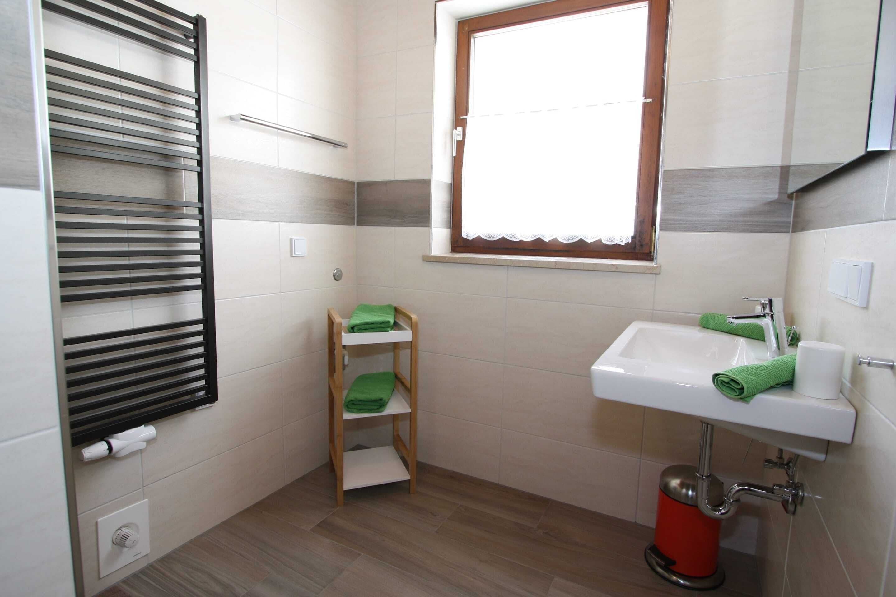 Un baño con toallero, ventana, lavamanos y un cubo de basura rojo.