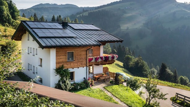 A chalet with a sloped roof, solar panels, and a balcony with flowers. - Apartment Near the ski Resort (Sankt Johann im Pongau)