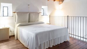Un dormitorio con techo de madera, una cama con cubrecama blanco, dos mesitas de noche y una ventana con cortina.