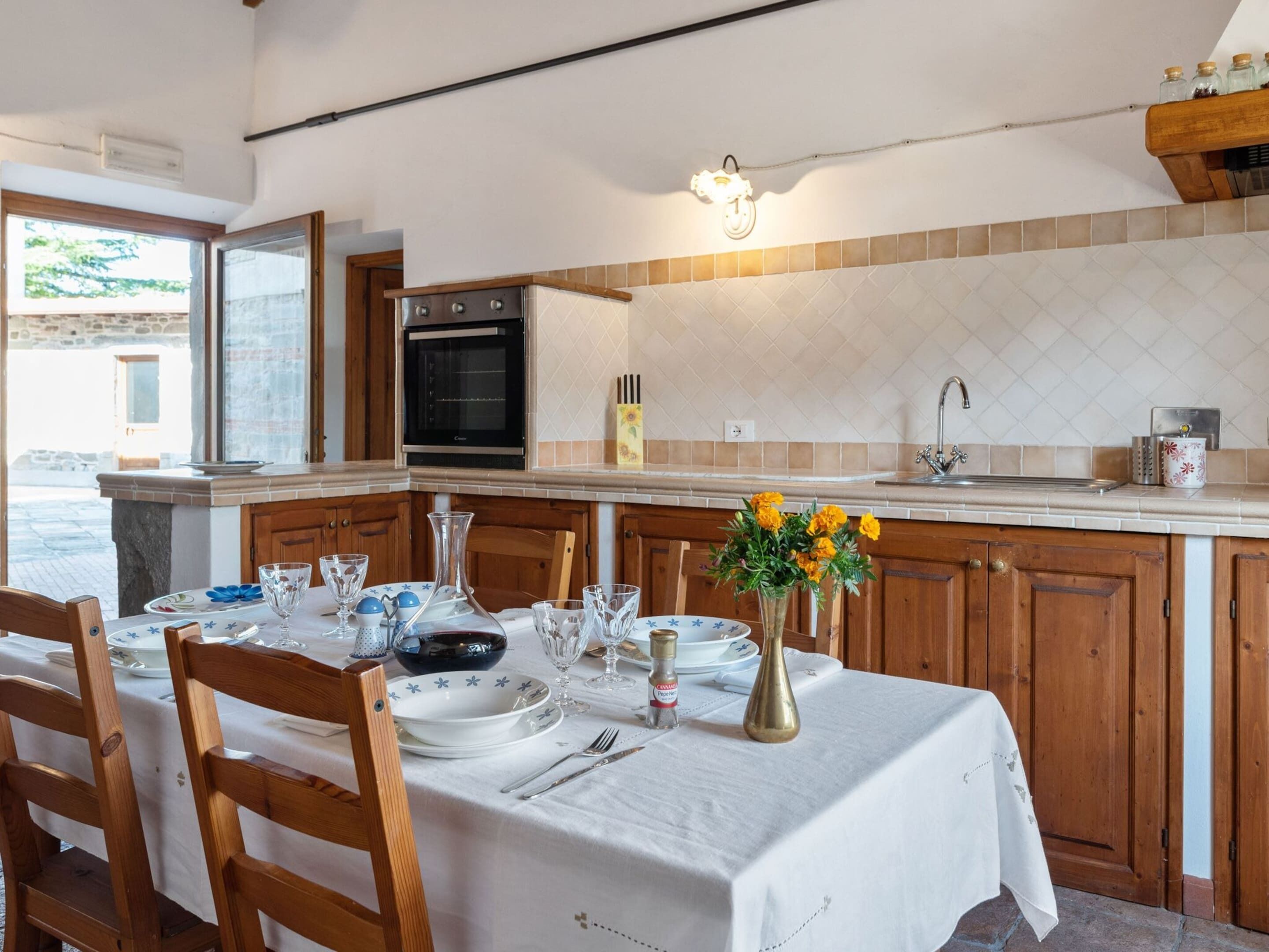 A dining area with a table set for four, a kitchen with wooden cabinets, a built-in oven, and a tiled backsplash.