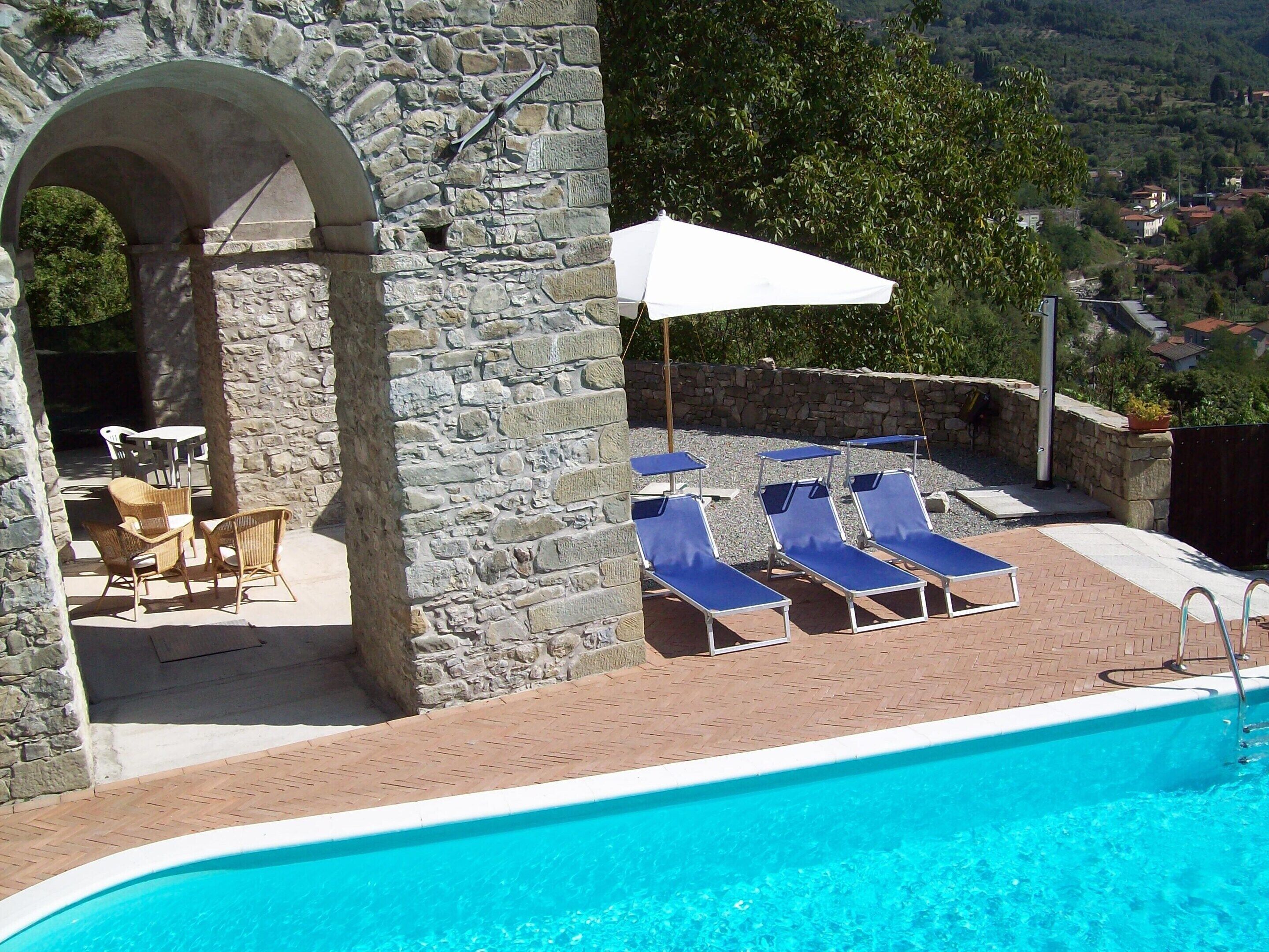 A pool area with lounge chairs, a table, and an umbrella.