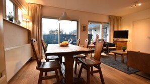 A dining area with a wooden table, chairs, a bowl of fruit, and a television in the background. - Comfortable Holiday Home in Bergen (Bergen)