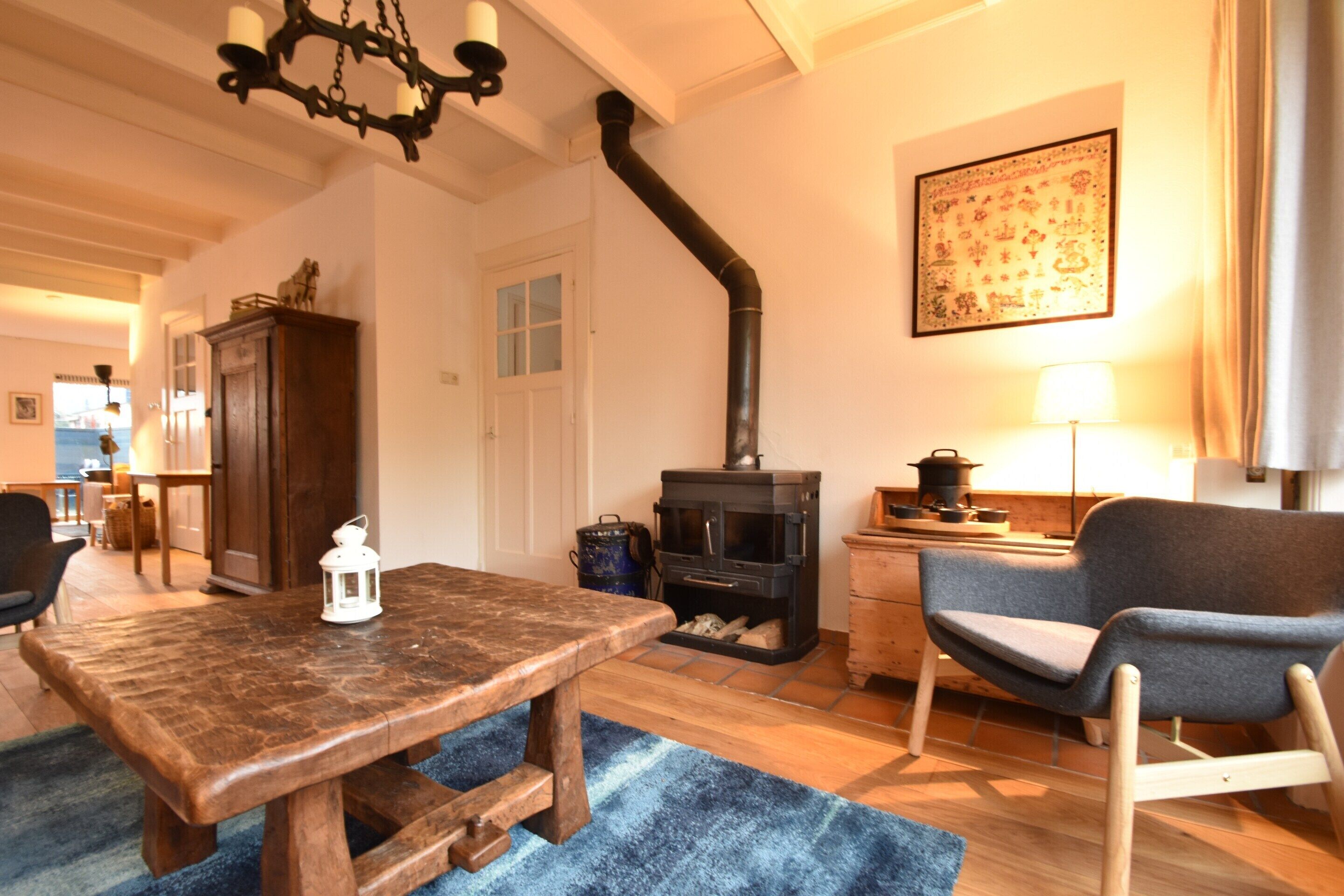 A cozy living room with a wooden table, a blue rug, a chair, a fireplace, and a lamp.