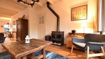 A cozy living room with a wooden table, a blue rug, a chair, a fireplace, and a lamp.