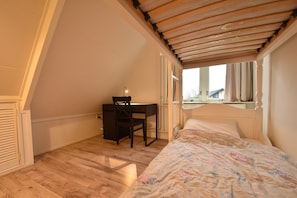 A bedroom with a sloped ceiling, a desk, a bed with a floral bedspread, and a window with curtains. - Comfortable Holiday Home in Bergen Near Forest (Bergen)
