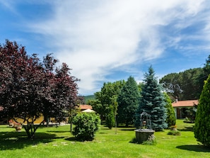 Un jardin bien entretenu, agrémenté de divers arbres, d’une fontaine en pierre et d’un bâtiment dont le toit est recouvert de tuiles rouges.