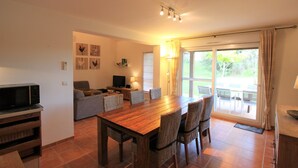 A dining area with a wooden table, wicker chairs, a sofa, and a television. - Provencal Parkside Haven (Arles)