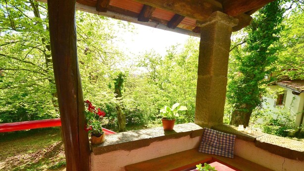 A covered outdoor seating area with a view of a lush garden and a building in the background. - Vintage Vacation Home (San Marcello Piteglio)