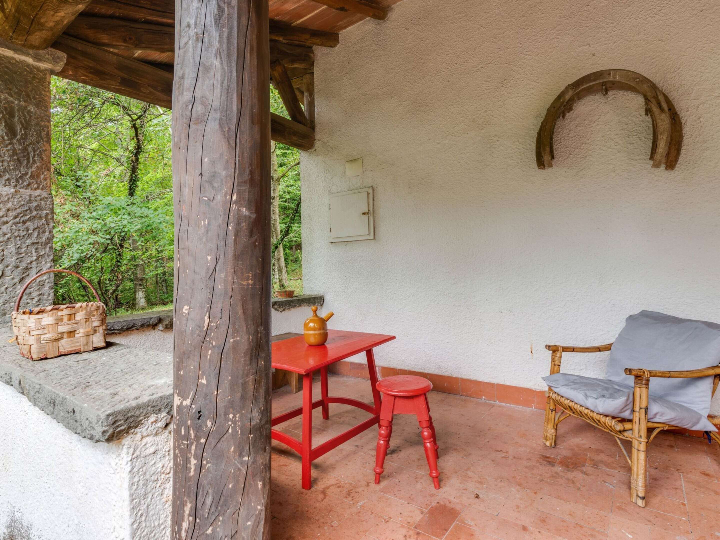 Un espacio de descanso al aire libre de estilo rústico, con una mesa y taburete rojos, una silla de mimbre y una cesta tejida.