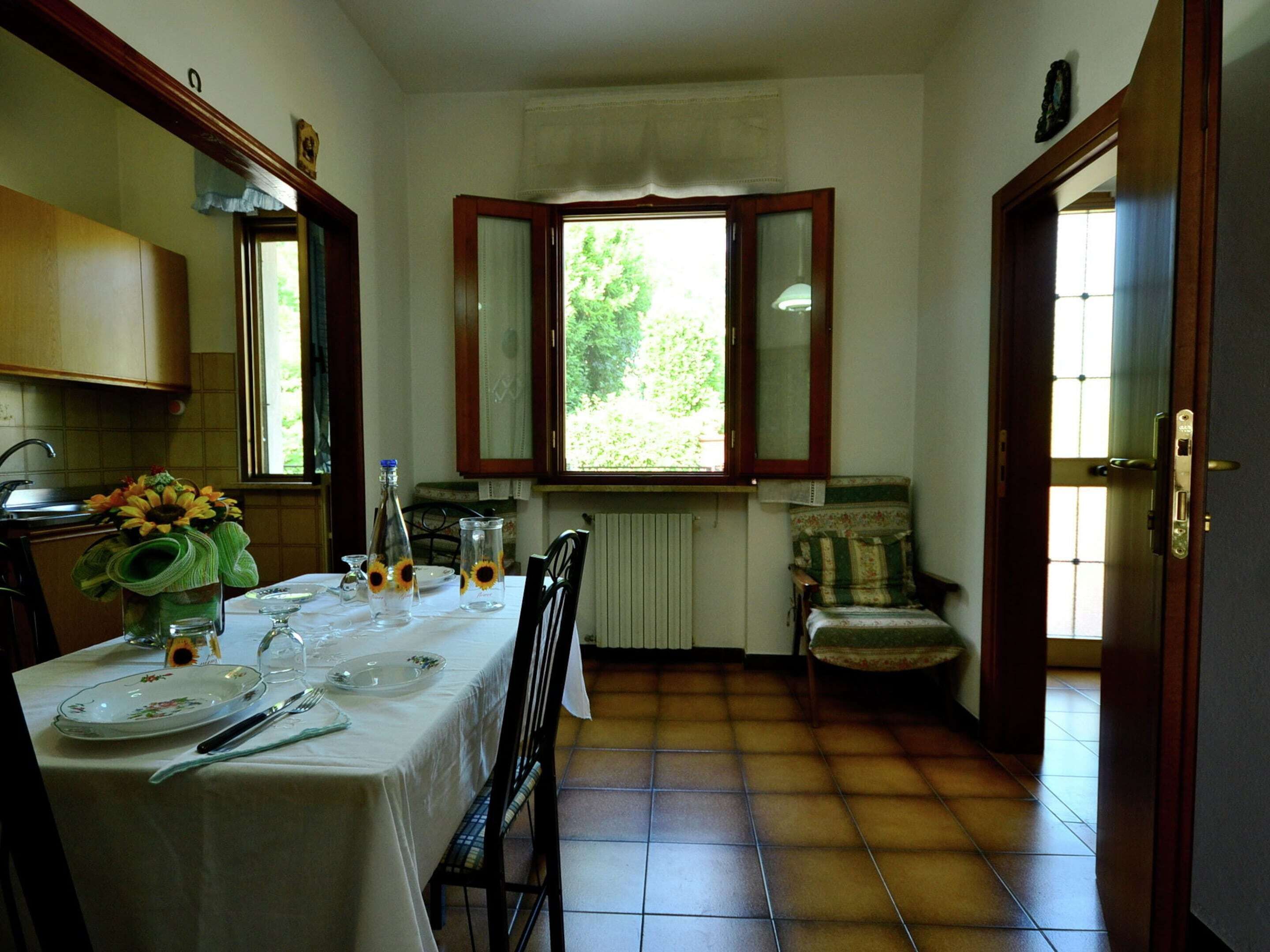 Un coin repas avec une table dressée pour quatre personnes, une chaise, un radiateur et une fenêtre donnant sur un paysage verdoyant.
