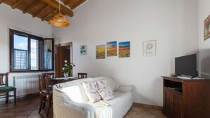 A cozy living room with a sofa, a dining table with chairs, a TV on a wooden cabinet, and artwork on the walls. - 360 Degree View of the Tuscan (Buonconvento)
