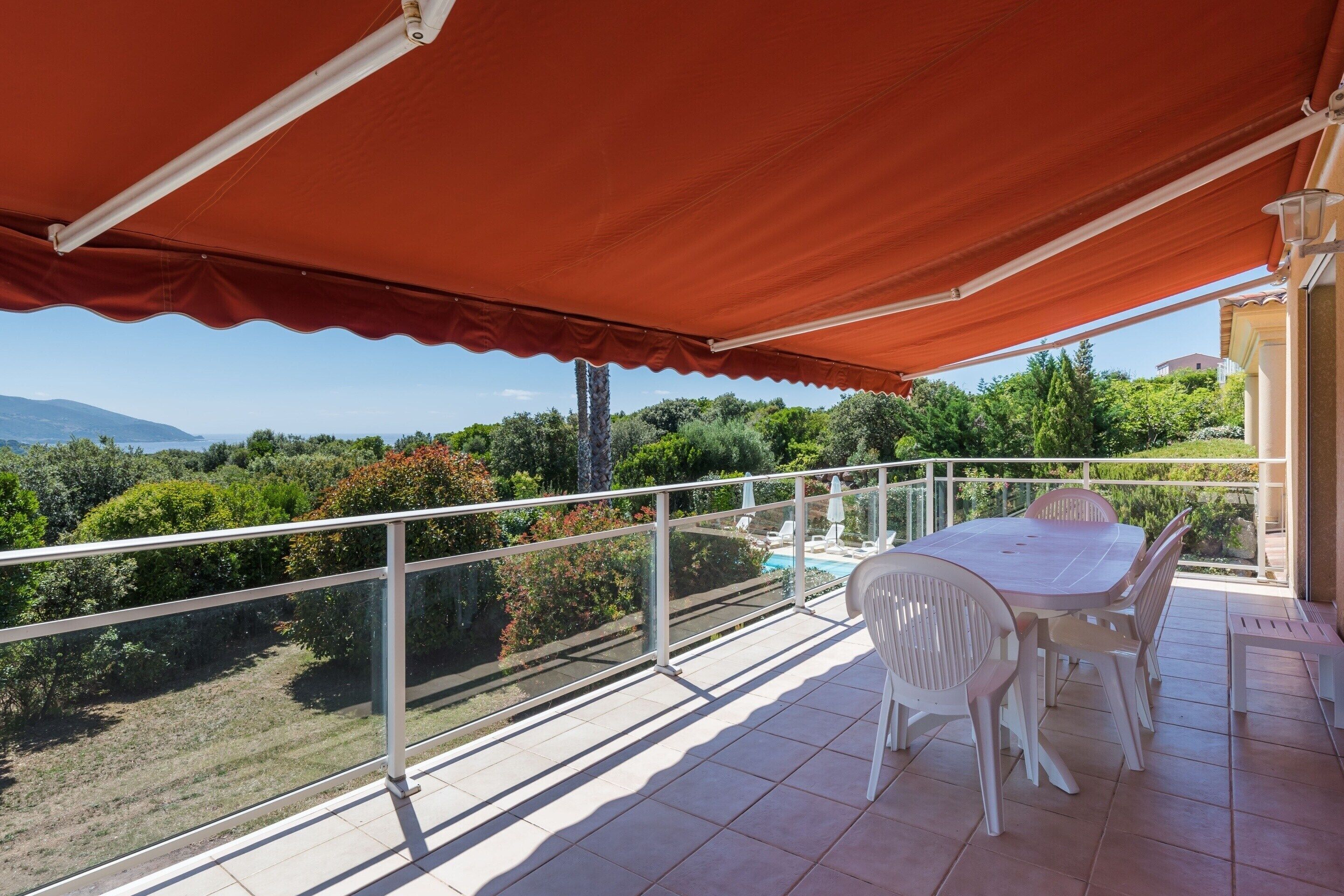 A balcony with a table and chairs, a pool, and a view of the landscape.