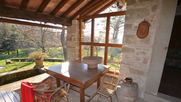 A rustic wooden table with wicker baskets, wicker chairs, and a stone wall with a window overlooking a garden. - Farmhouse in Mugello With Valley Views (Borgo San Lorenzo)