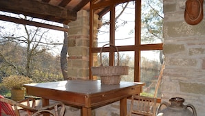 A rustic wooden table with a basket, two wicker chairs, and a large ceramic pot in a stone-walled room with large windows. - Farmhouse in Mugello With Valley Views (Borgo San Lorenzo)