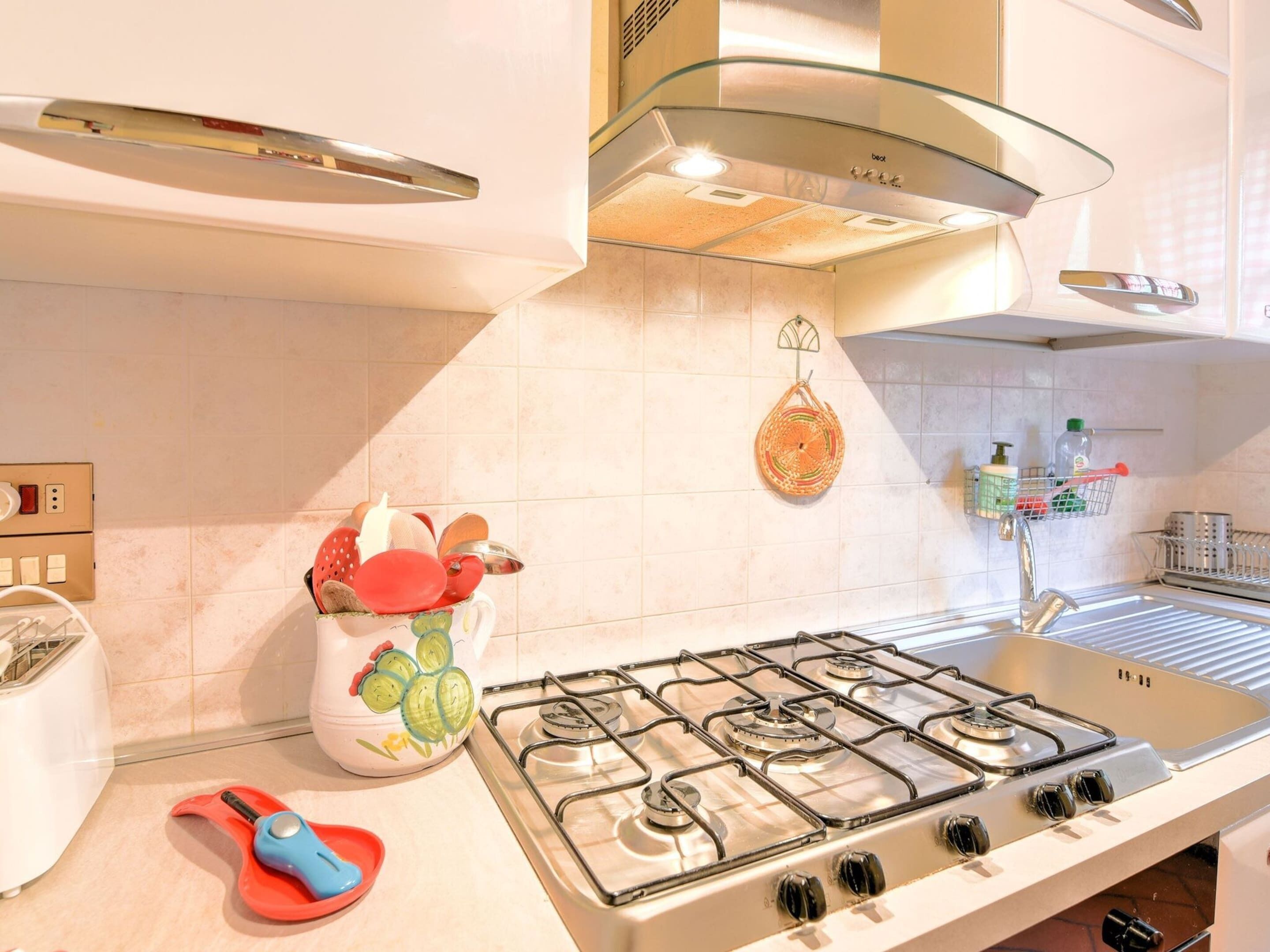 A kitchen with a gas stove, a toaster, and a hanging basket with fruits.