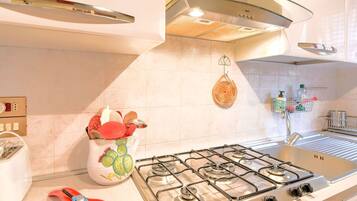 A kitchen with a gas stove, a toaster, and a hanging basket with fruits.