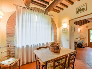 A dining area with a brick wall, a table with chairs, and a window with curtains. - Scenic Stay in Restored Retreat (Monterchi)