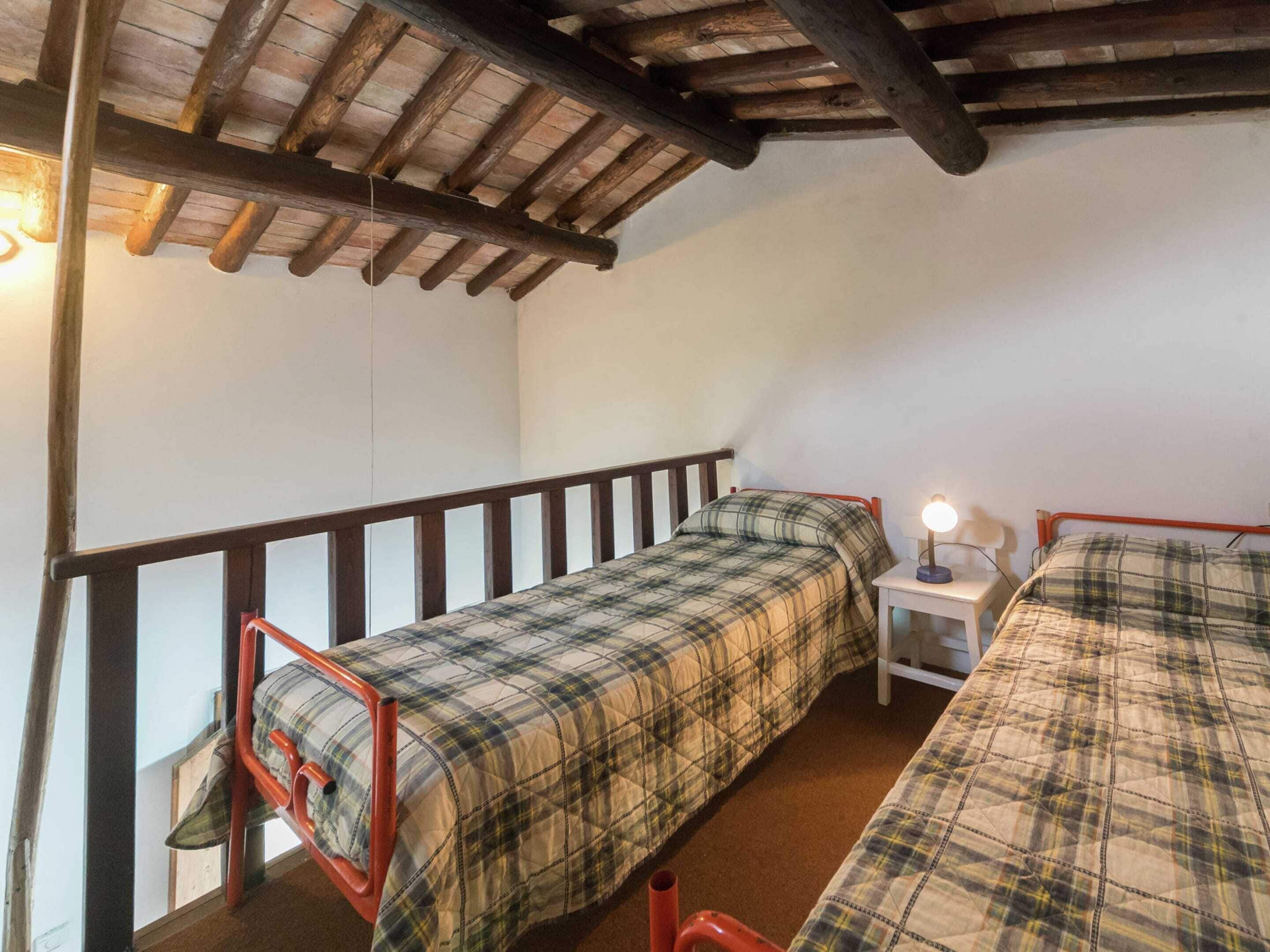 Quarto de dormitório com duas camas individuais, uma pequena mesa de cabeceira com luminária e teto de madeira.