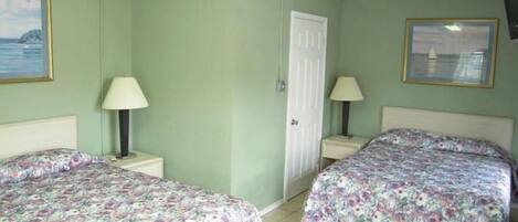 Una habitación con dos camas, cada una con una colcha estampada, dos lámparas de noche, una puerta blanca y un cuadro en la pared.