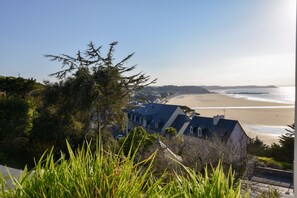 A coastal view with a beach, a house with a blue roof, and greenery in the foreground. - Seaside Comfort in Erquy (Erquy)