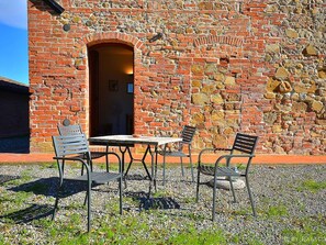 An outdoor seating area with a table and four chairs in front of a stone wall with a brick archway. - Peccioli Family Retreat (Peccioli)