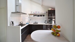 Une cuisine moderne avec des meubles blancs, une hotte en acier inoxydable et un présentoir à fruits.