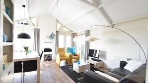 Un salon moderne avec un canapé en cuir noir, une table basse blanche, un fauteuil jaune et un téléviseur posé sur un meuble blanc.