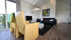Un salon moderne avec un canapé jaune, un canapé noir, un téléviseur à écran plat et un tableau accroché au mur.