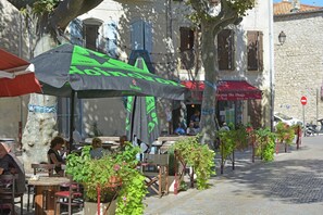 Terrasse mit Tischen und Stühlen, eine Kopfsteinpflasterstraße und ein Gebäude mit einer Stein-Fassade.
