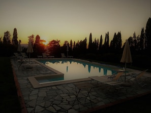A swimming pool with lounge chairs and umbrellas, surrounded by trees and a sunset in the background. - Tuscan Charm Near Volterra (Volterra)