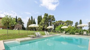 A swimming pool with lounge chairs and umbrellas, surrounded by greenery and a building in the background. - Tuscan Charm Near Volterra (Volterra)