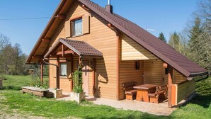 Una cabana de fusta amb teulada a dos vessants, una xemeneia i un petit porxo amb una taula i cadires.