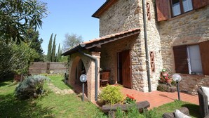 A stone house with a wooden balcony, a garden with potted plants, and a clear blue sky. - Charming Villa in Suvereto with Hot Tub (Suvereto)