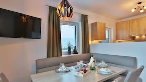 Un espace repas moderne avec une table en bois disposée pour quatre personnes, un téléviseur fixé au mur et une vue sur l’extérieur par une fenêtre.