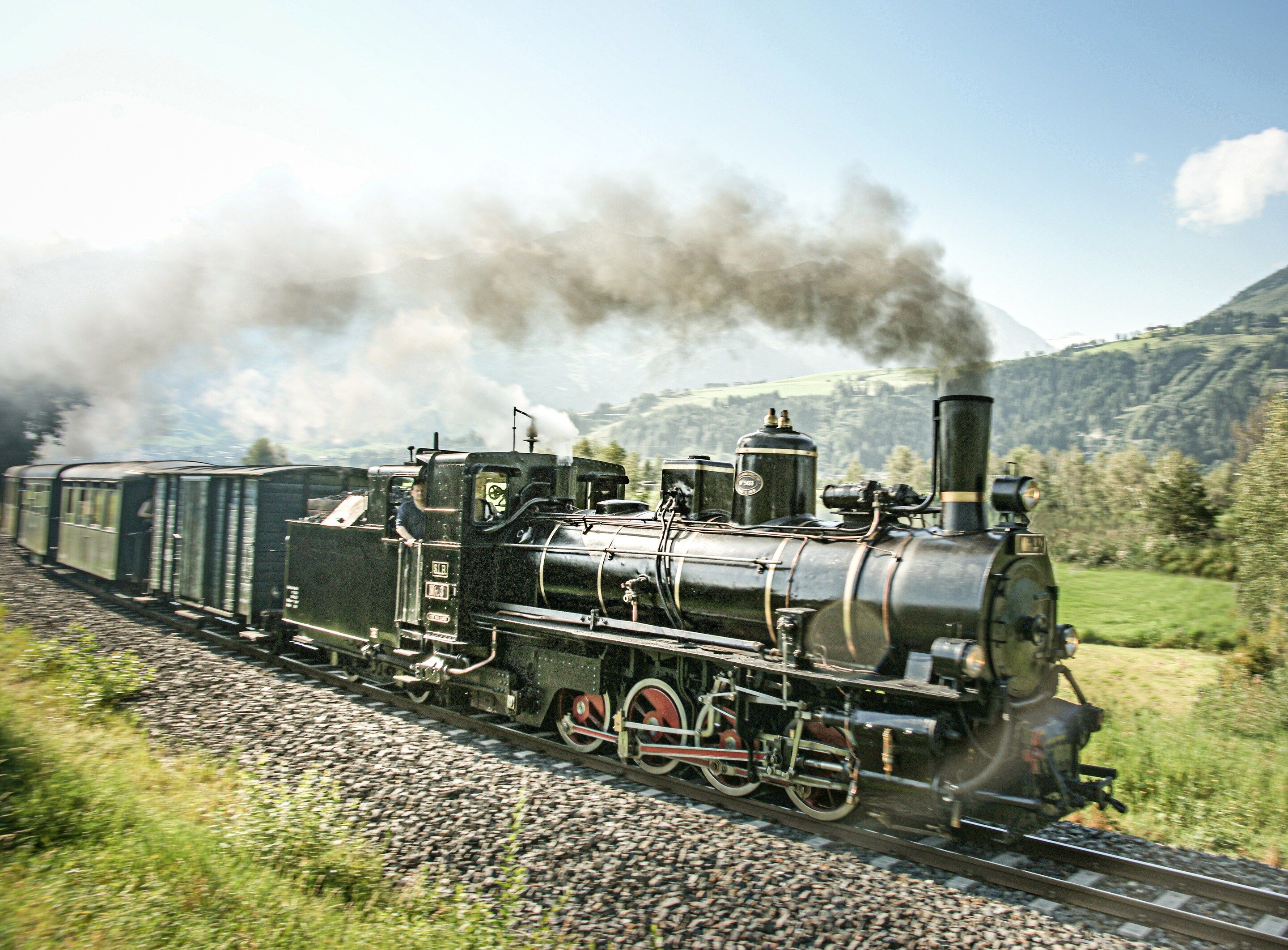 A steam locomotive with multiple passenger cars on a railway track.