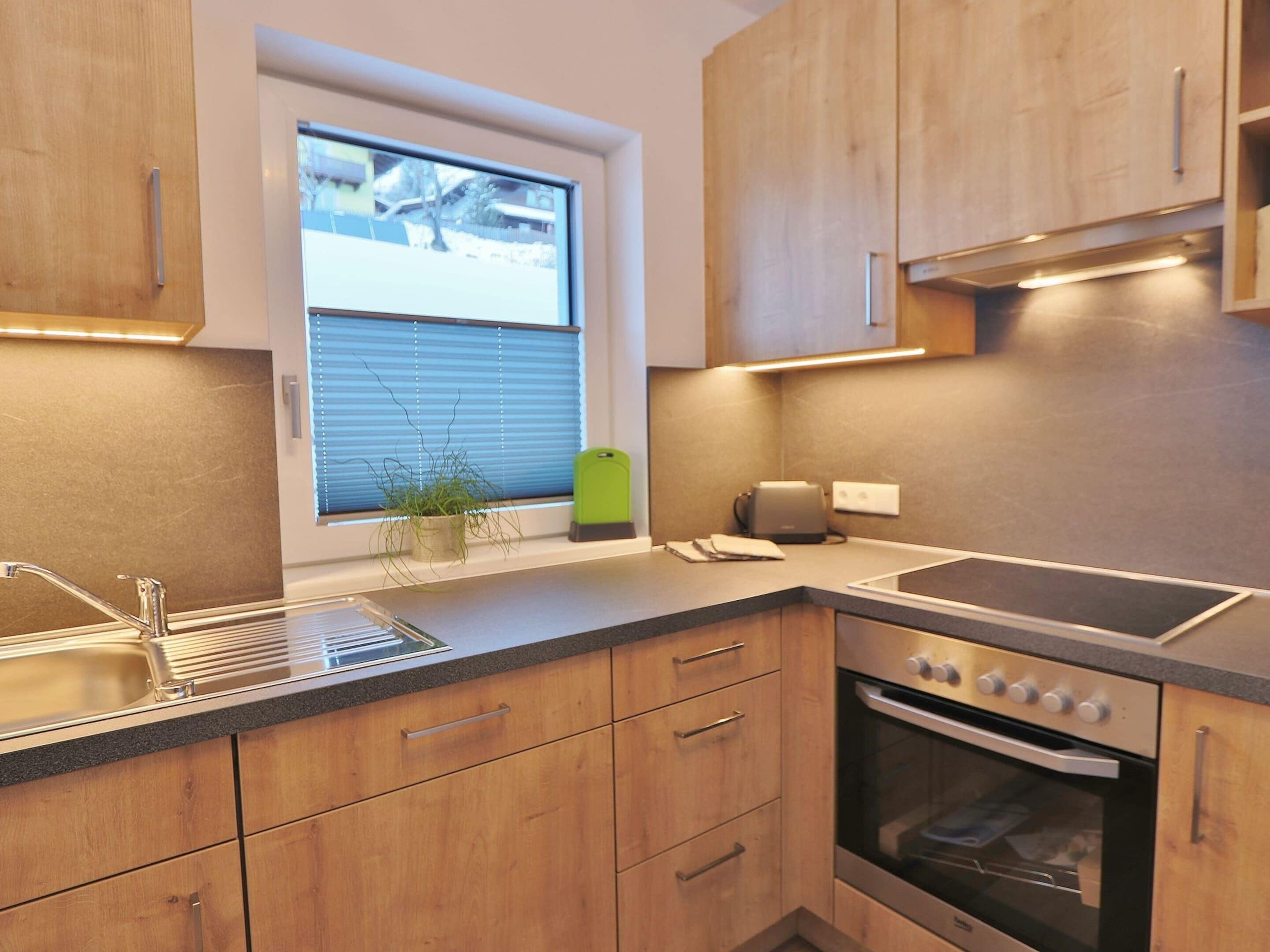 Una cocina moderna con armarios de madera, horno empotrado, lavabo y ventana con persianas.