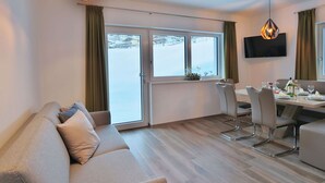Un salon moderne comprenant un canapé, une table à manger, des chaises et un téléviseur fixé au mur.