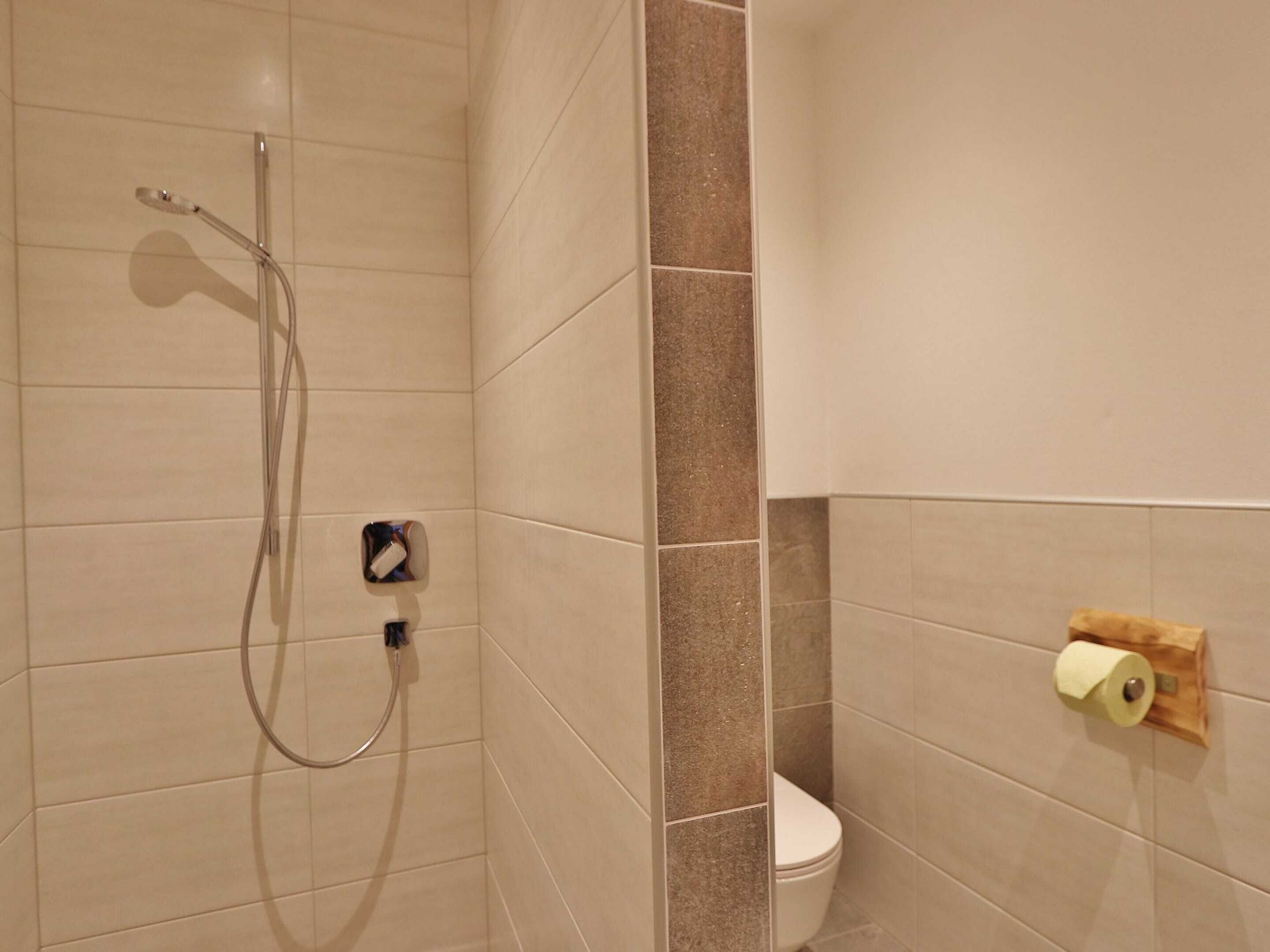 A bathroom with a shower, toilet, and a paper towel dispenser.