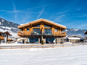 A two-story wooden chalet with a balcony, set against a snowy mountain backdrop. - Holiday Home in Niedernsill With Sauna (Niedernsill)